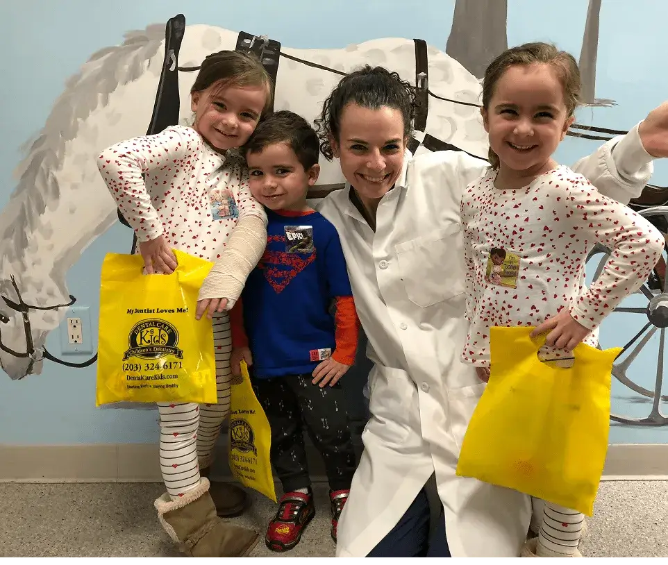 Three happy kids with their dentist holding goodie bags at Dental Care Kids